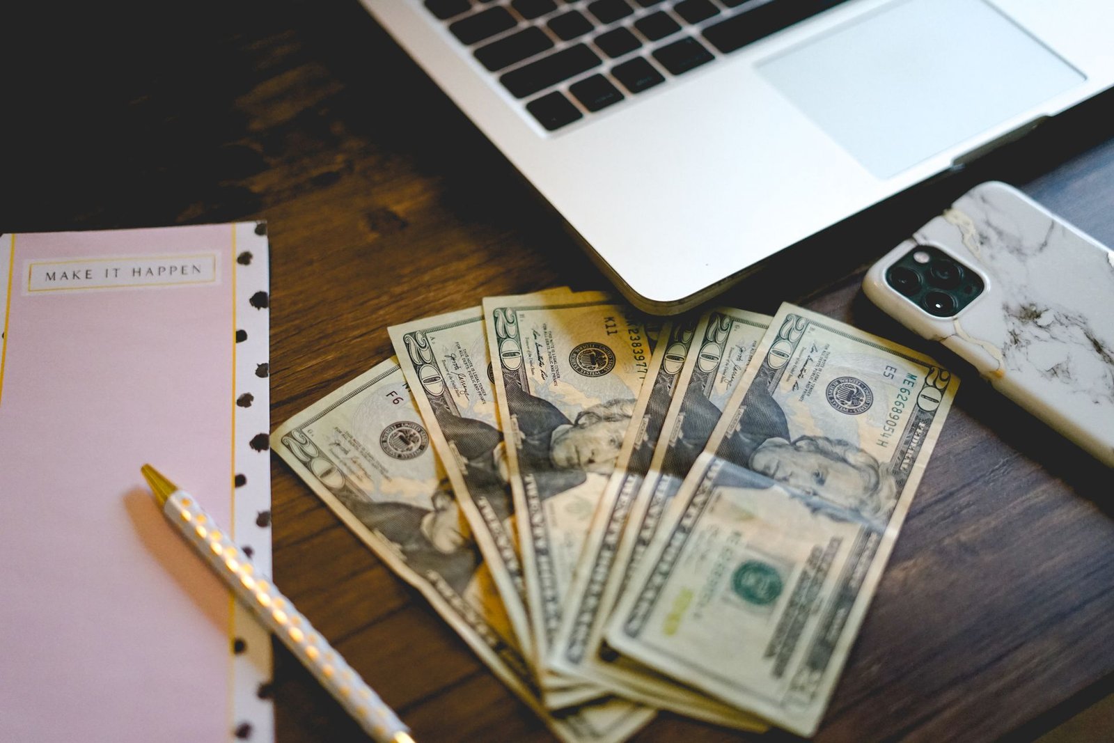 Laptop, smartphone, notebook, and cash representing ways to make money blogging