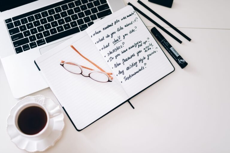 A laptop, notebook with handwritten notes, and coffee on a desk