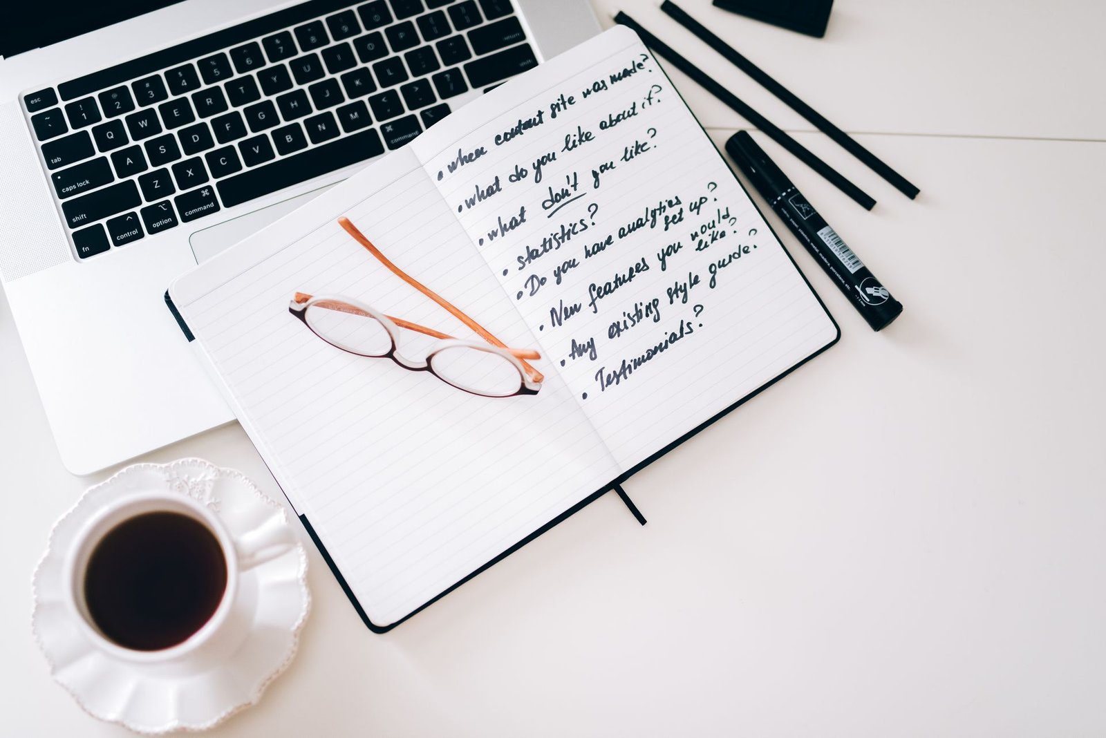 A laptop, notebook with handwritten notes, and coffee on a desk